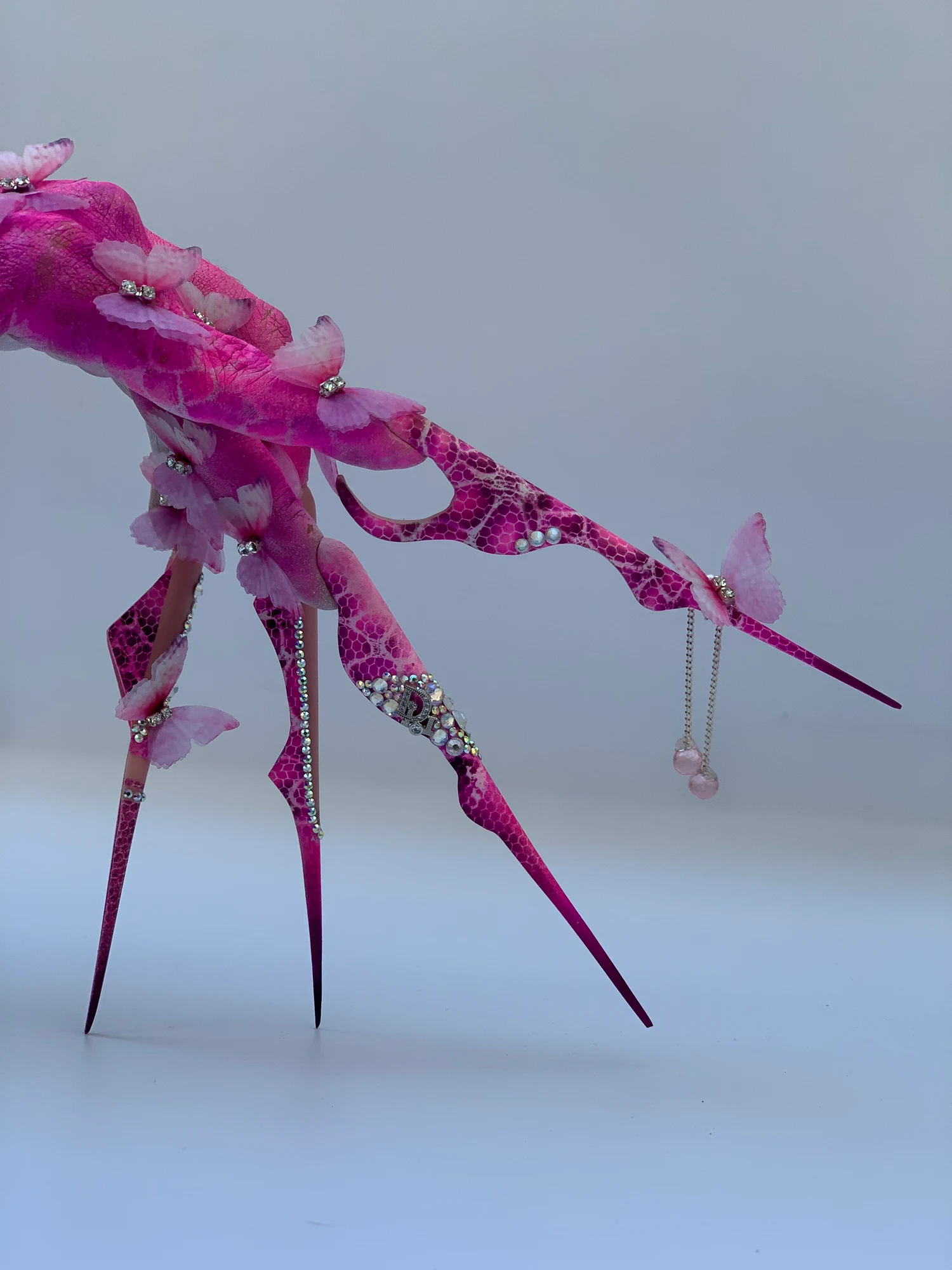 Composición de cuatro uñas extremas fucsias con mariposas y pedrería sobre fondo claro