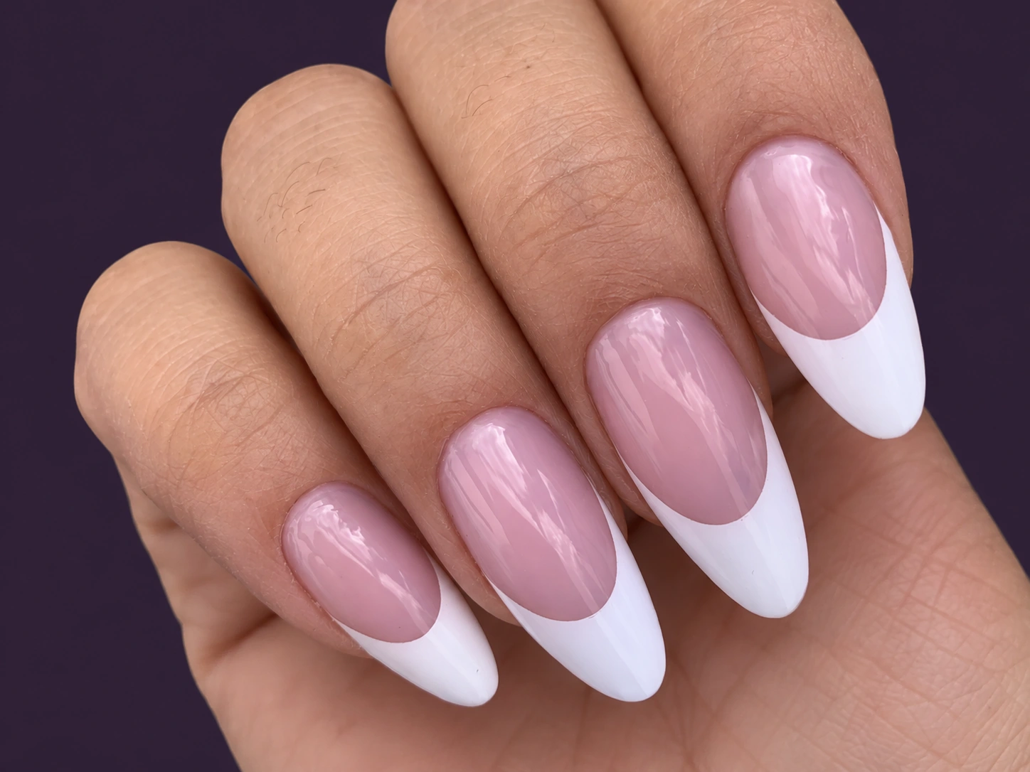 Manicura francesa rosa y blanca de Apres Gel X sobre fondo ciruela oscuro