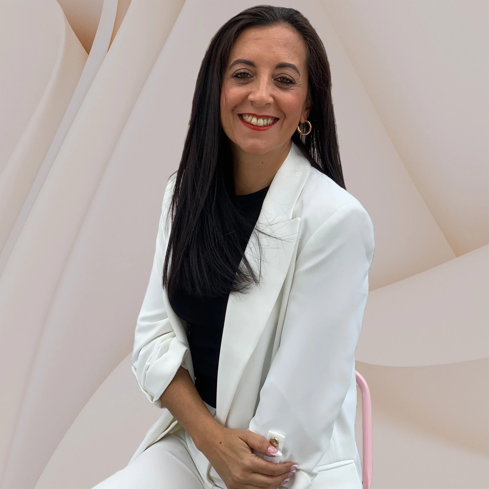 Sara Orozco con chaqueta blanca, sentada en un sillón rosa
