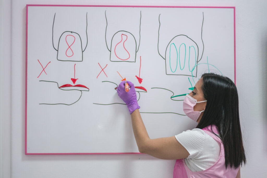 Sara Orozco explica esquemas de uñas en una pizarra durante una clase de manicura