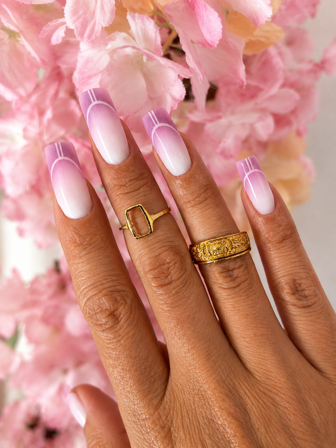 Uñas de Sistema Dual con acabado rosa y blanco, sobre un fondo de flores rosas.
