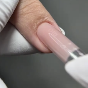 Forma superior transparente con producto rosa sobre una uña natural, sostenida con guantes blancos.