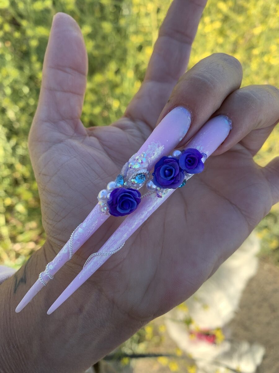 Dos uñas stiletto rosas con flores violetas, perlas y pedrería