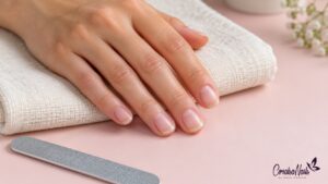 Mano con uñas naturales cortas y sin esmalte sobre una toalla clara, junto a una lima.