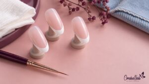 Tres tips de práctica con base rosa y punta francesa blanca junto a un pincel fino.