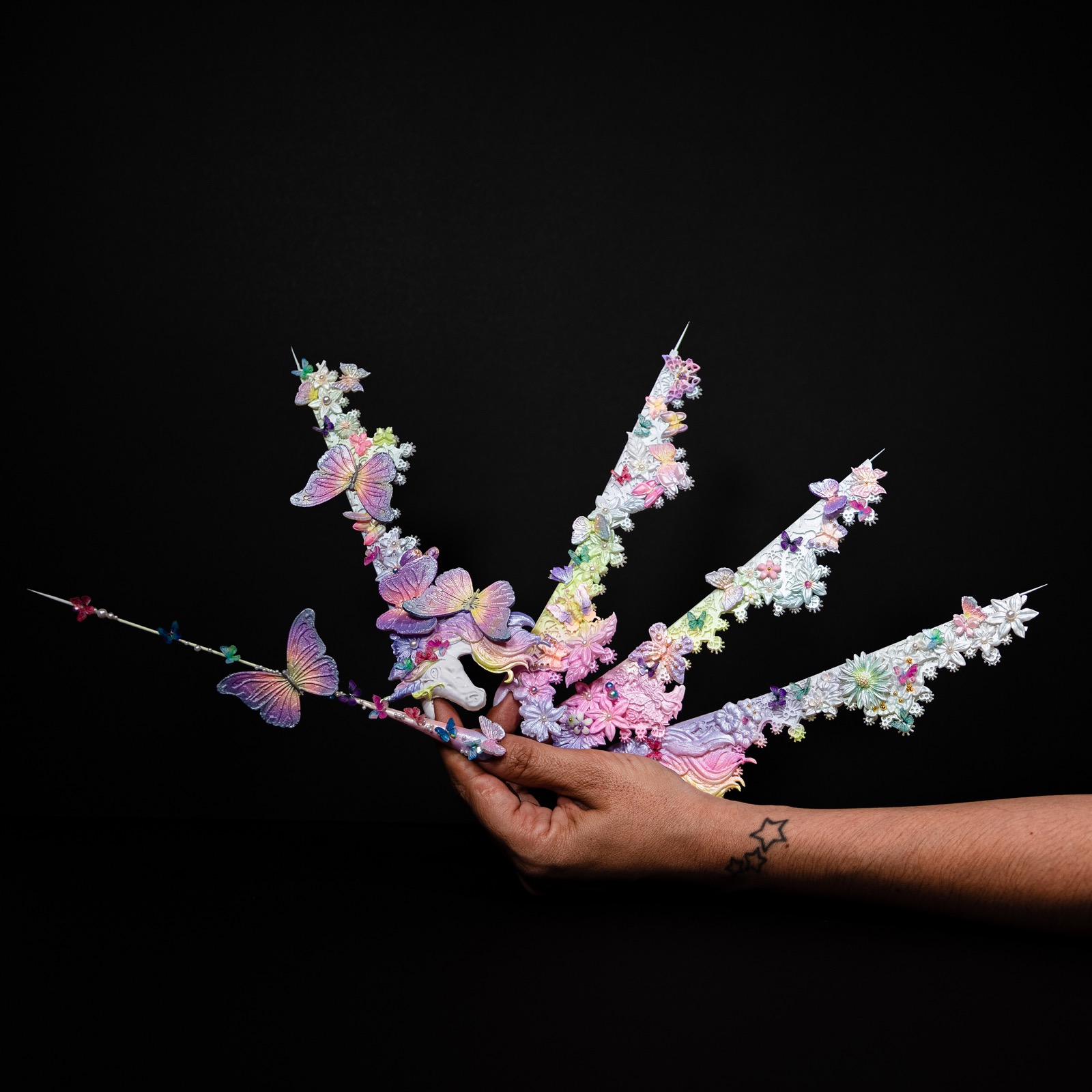 Composición artística de uñas decoradas con flores y mariposas sostenida con una mano