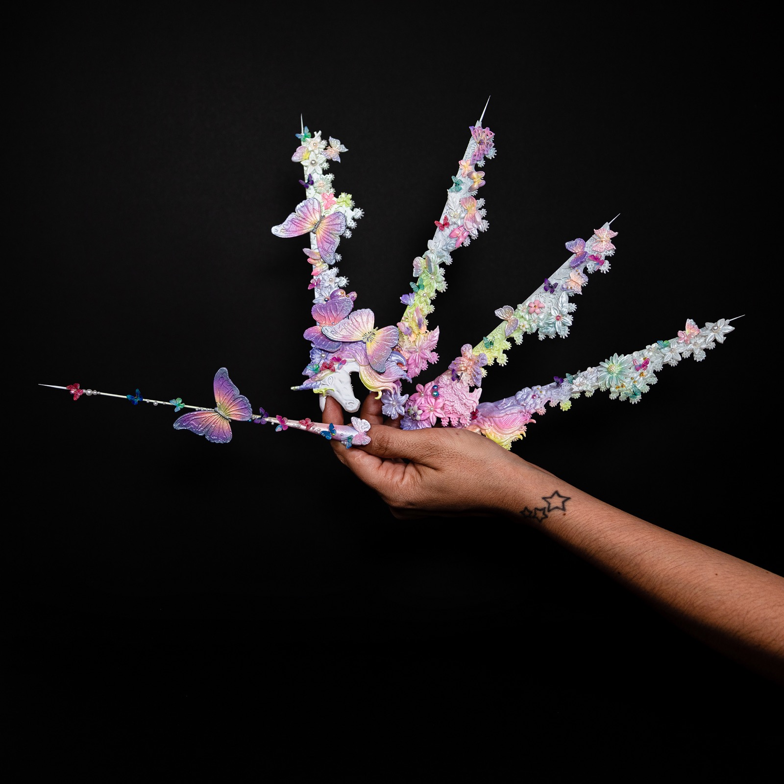Vista completa de una pieza artística de uñas con detalles florales y mariposas sobre fondo negro