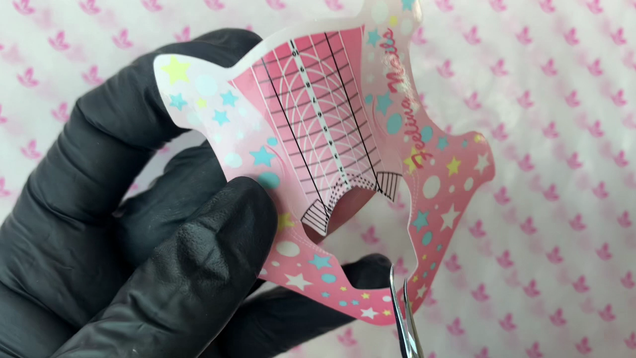 Tijeras junto al lateral de un molde adhesivo rosa durante su ajuste, con el molde fuera del dedo.