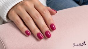 Primer plano de una manicura fucsia con el color dentro del contorno de las uñas.