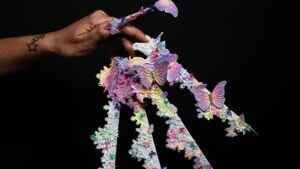 Mano junto a una composición artística de uñas con mariposas sobre fondo negro